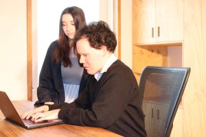 Man with disability sitting at a computer with support professional