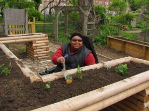 Woman in a chair sitting behind a garden bed holding a small shovel