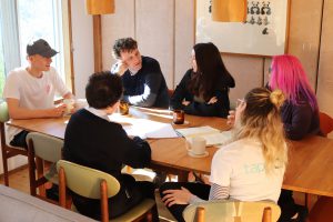 Six individuals sitting around an oval table discussing a topic.